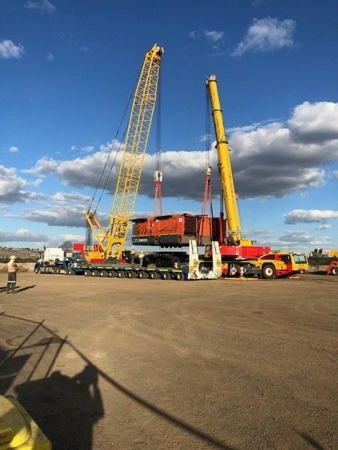 A Large Yellow Crane Is Lifting A Container In A Parking Lot — SureLift Crane Hire In Moranbah, QLD