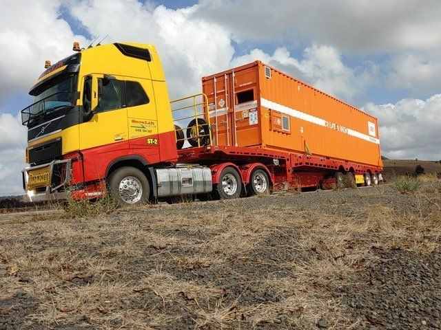A Yellow And Red Semi Truck Is Carrying An Orange Shipping Container — SureLift Crane Hire In Moranbah, QLD