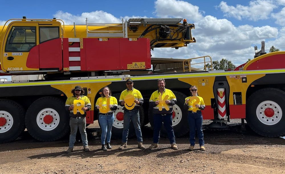A Group Of Workers Are Standing In Front Of A Large Crane — SureLift Crane Hire In Bowen, QLD