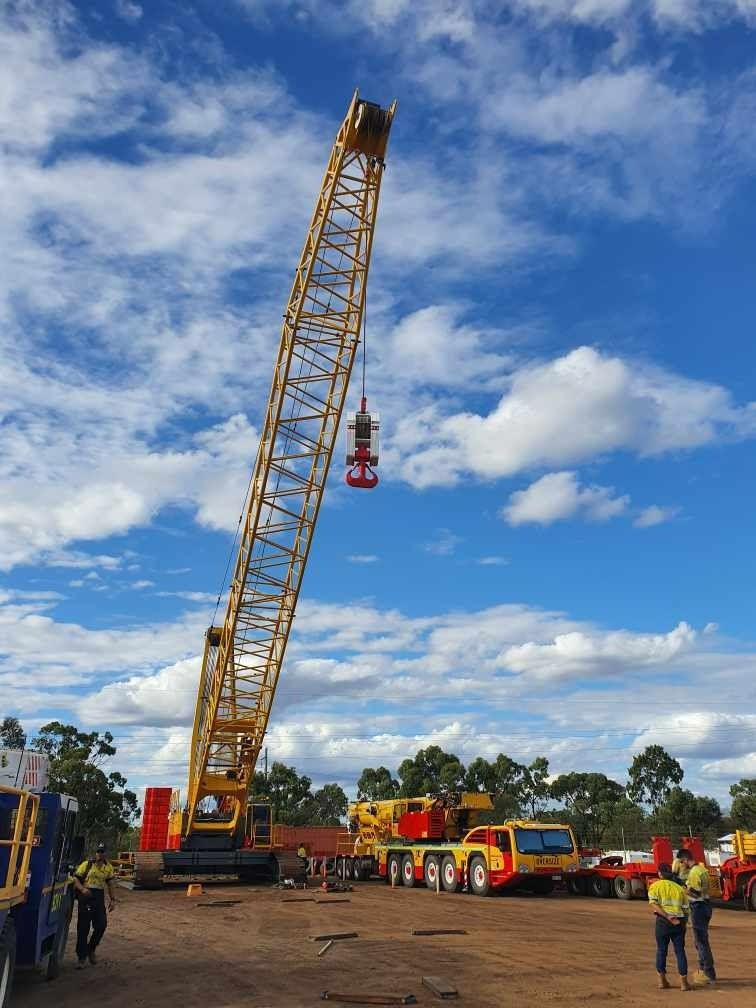 A Large Yellow Crane Is Lifting A Red Object In A Dirt Field — SureLift Crane Hire In Bowen, QLD
