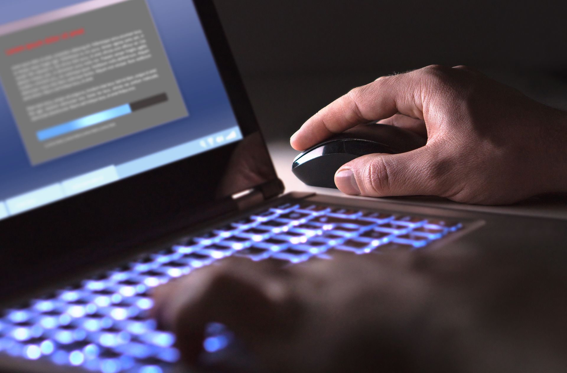 Person using laptop with glowing keyboard and mouse, screen showing text and progress bar.