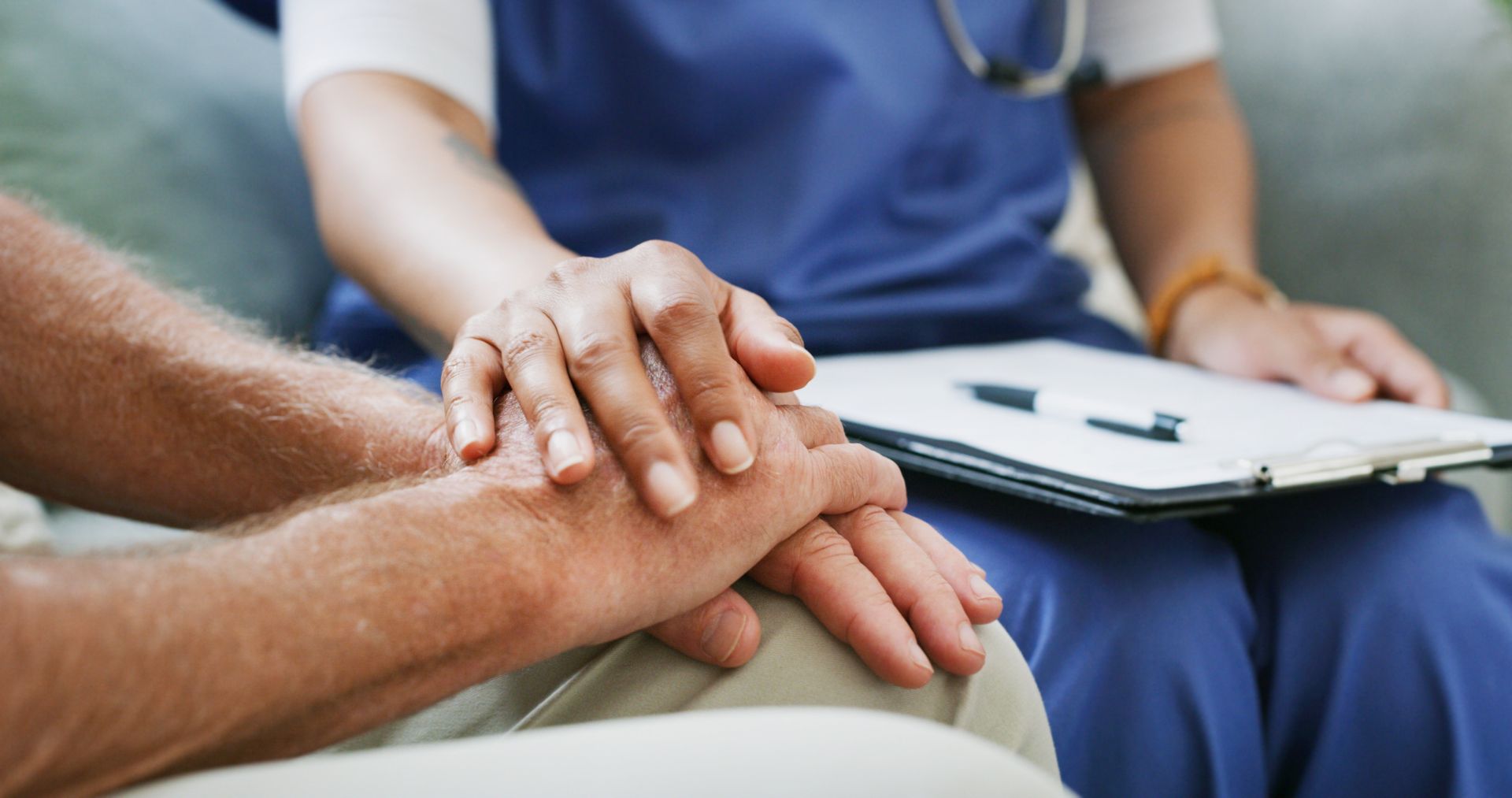 Nurse's hand comforting patient's hands while holding a clipboard