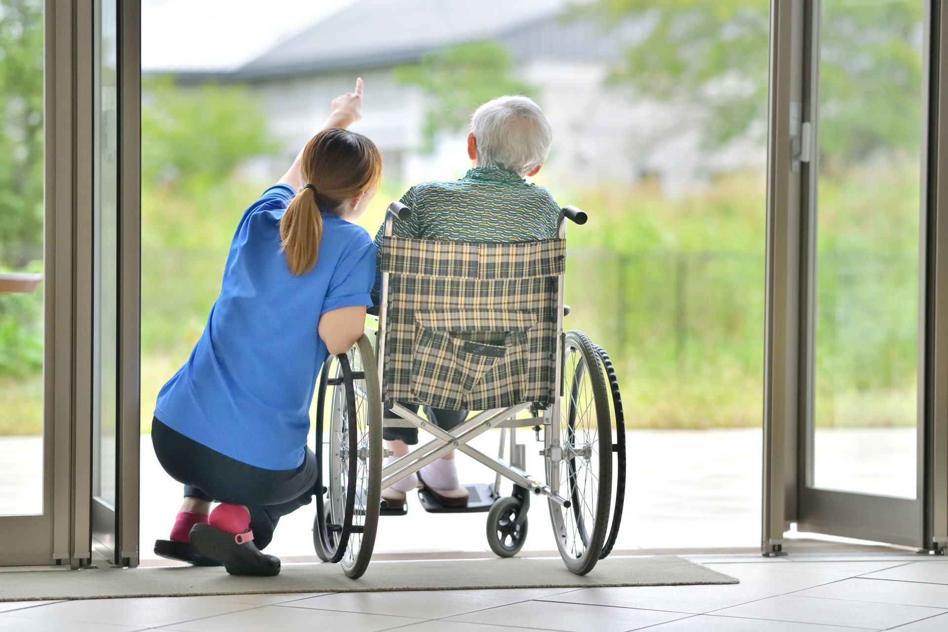 Caregiver points upward, assisting person in wheelchair to look out open doorway