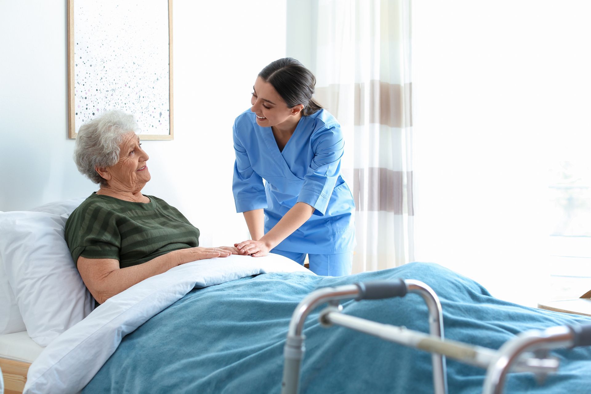 Nurse tending to an elderly person in bed with a walker nearby Nurse tending to an elderly person in bed with a walker nearby
