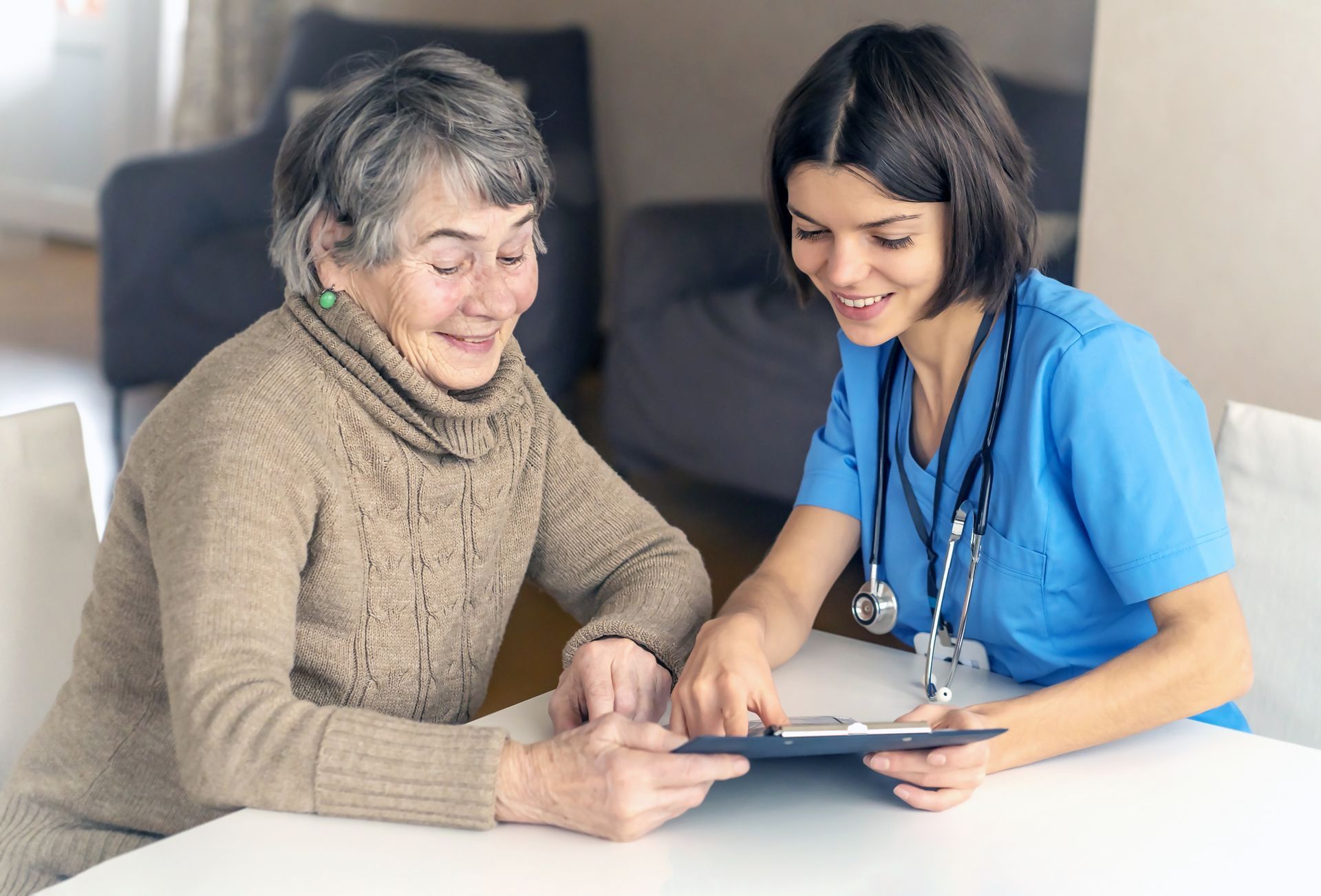 Woman and healthcare worker smiling, reviewing documents at a table. Blue scrubs, stethoscope visible