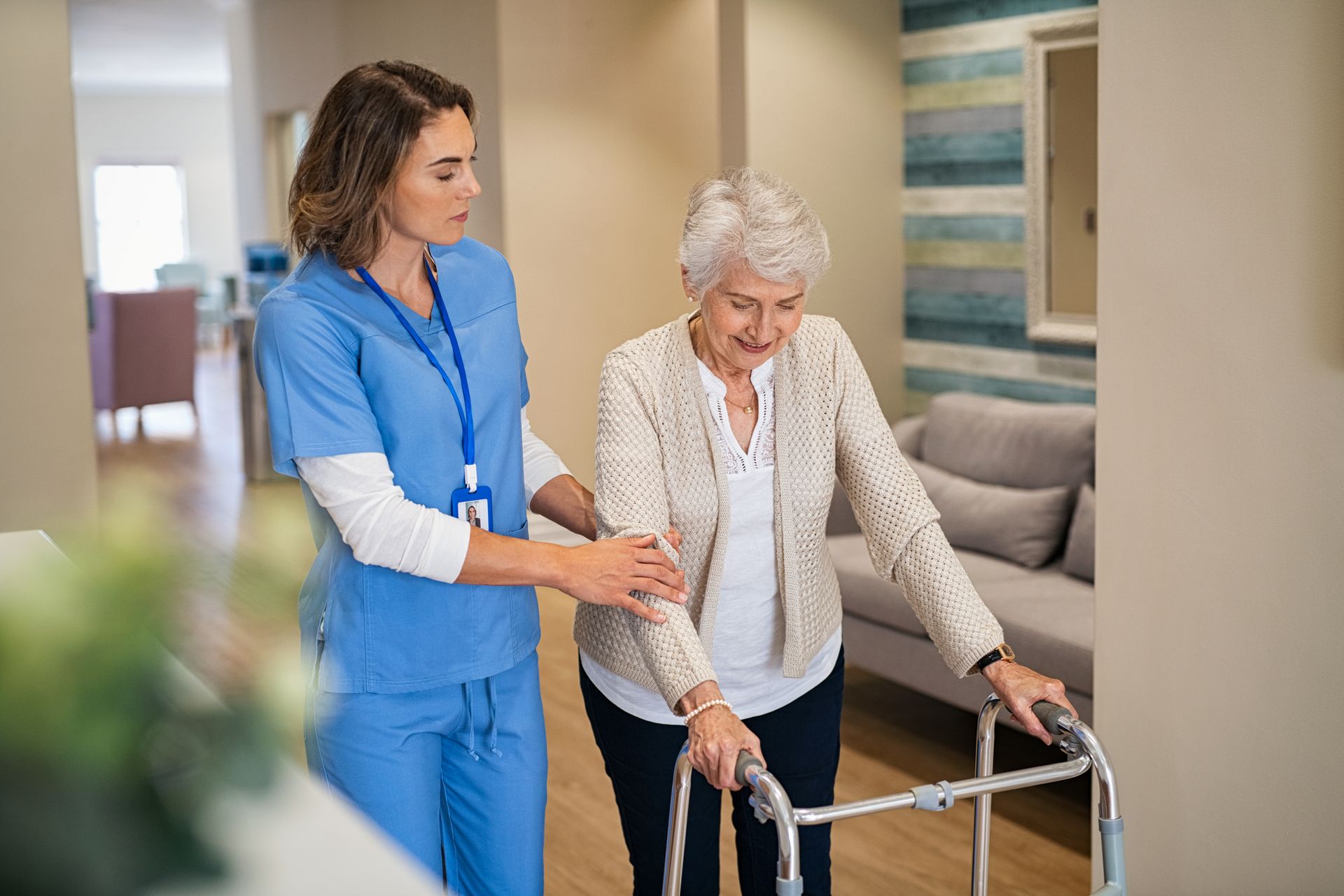 Nurse assisting a person using a walker in a hallway. Both are smiling
