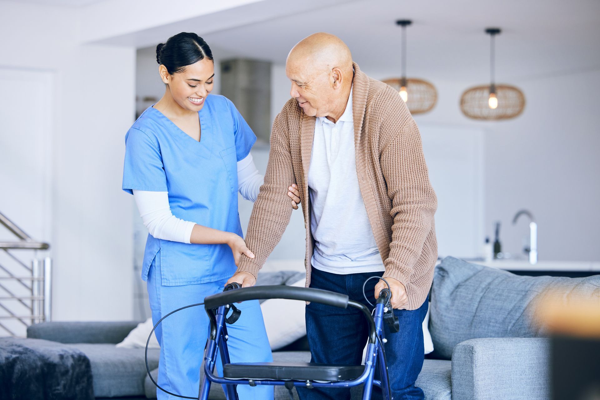 Nurse assists an older person with a walker in a home. The nurse wears blue scrubs and smiles Nurse assists an older person with a walker in a home. The nurse wears blue scrubs and smiles