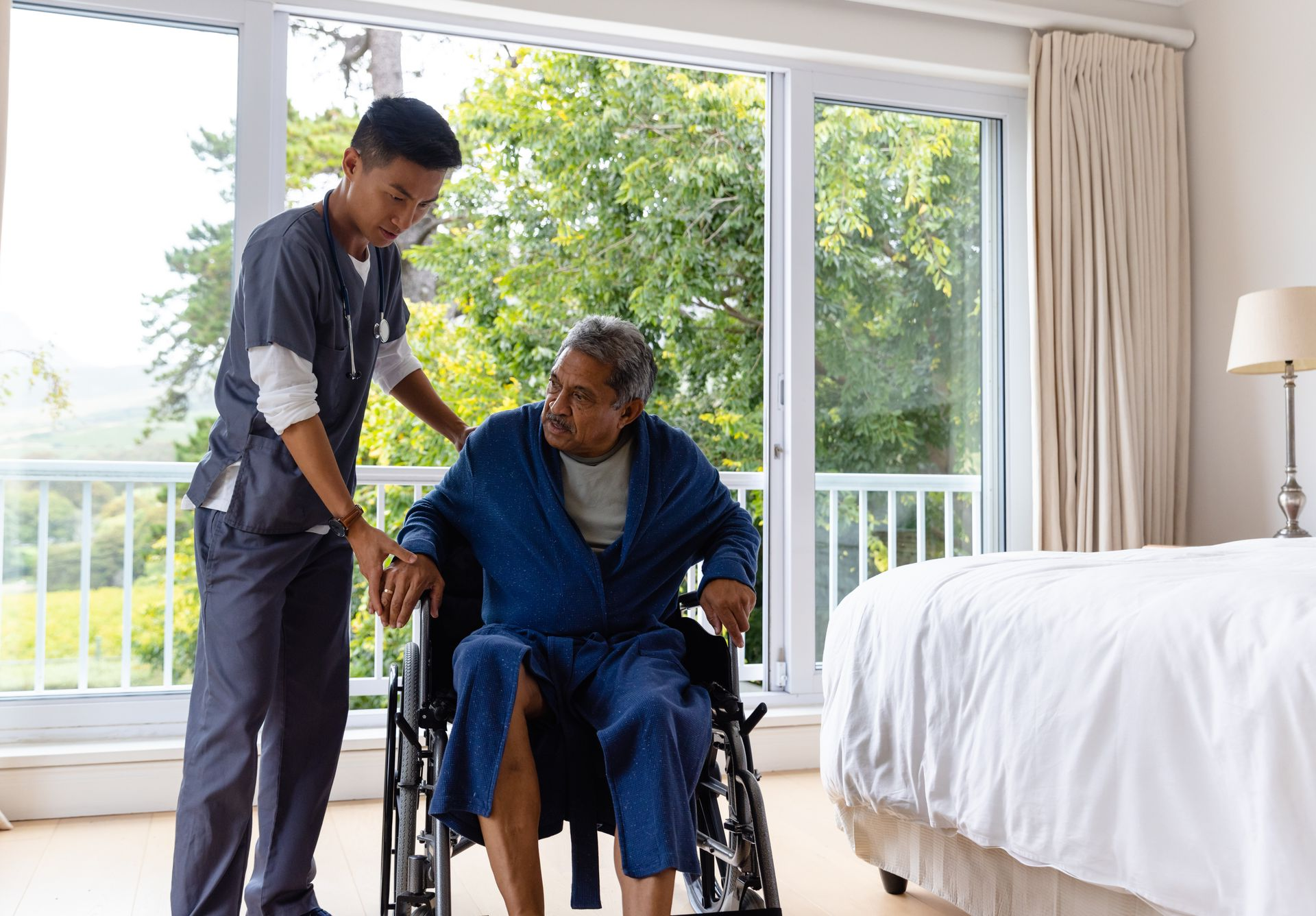 Caregiver assisting a person using a walker in a room; the caregiver wears blue scrubs Caregiver assisting a person using a walker in a room; the caregiver wears blue scrubs