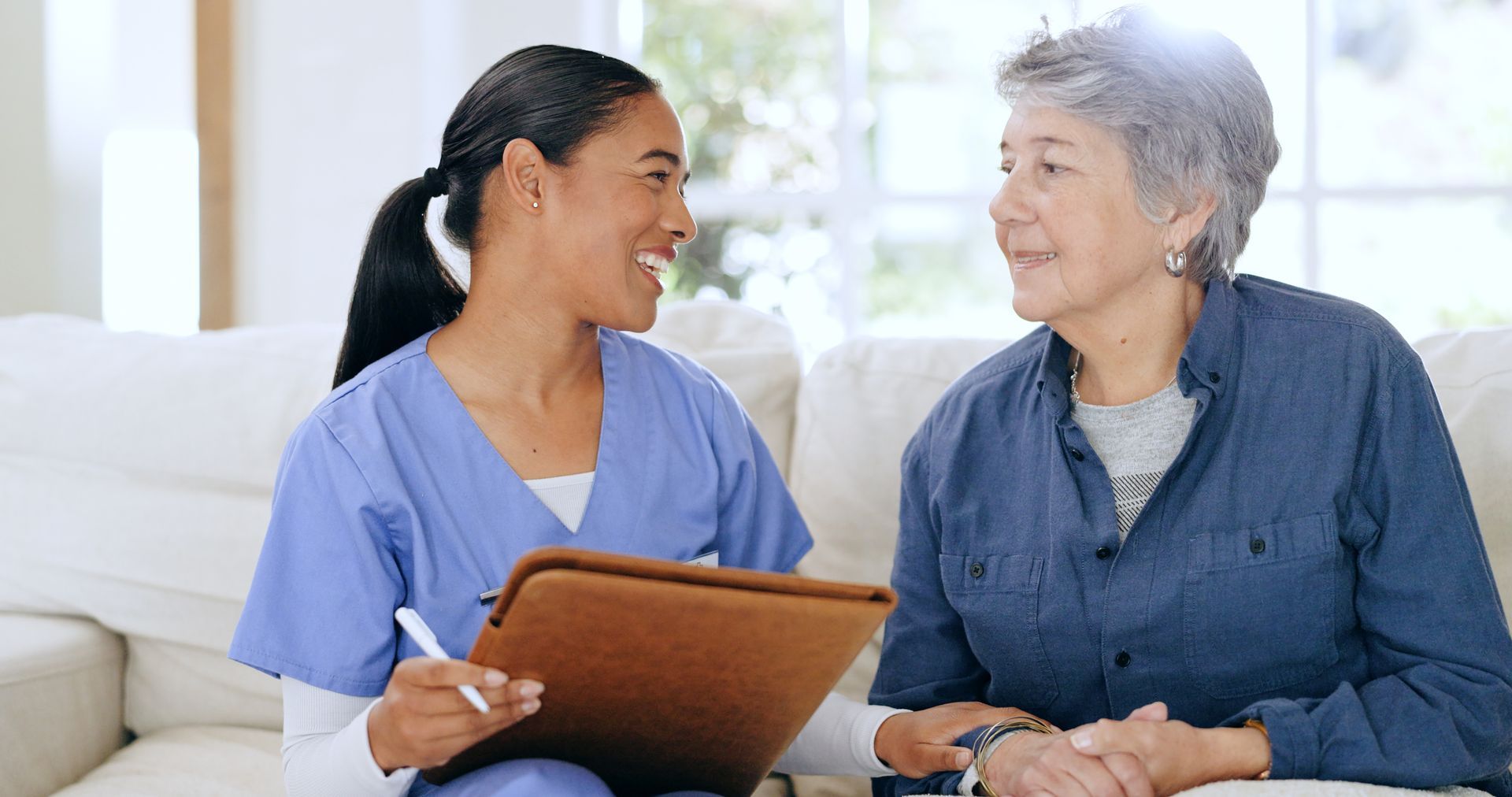 Nurse in blue scrubs consulting with a patient seated on a couch, holding a clipboard Nurse in blue scrubs consulting with a patient seated on a couch, holding a clipboard