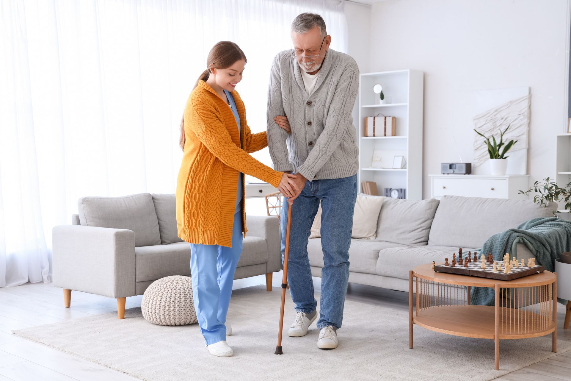 Woman in yellow cardigan helps man with cane walk in a living room Woman in yellow cardigan helps man with cane walk in a living room