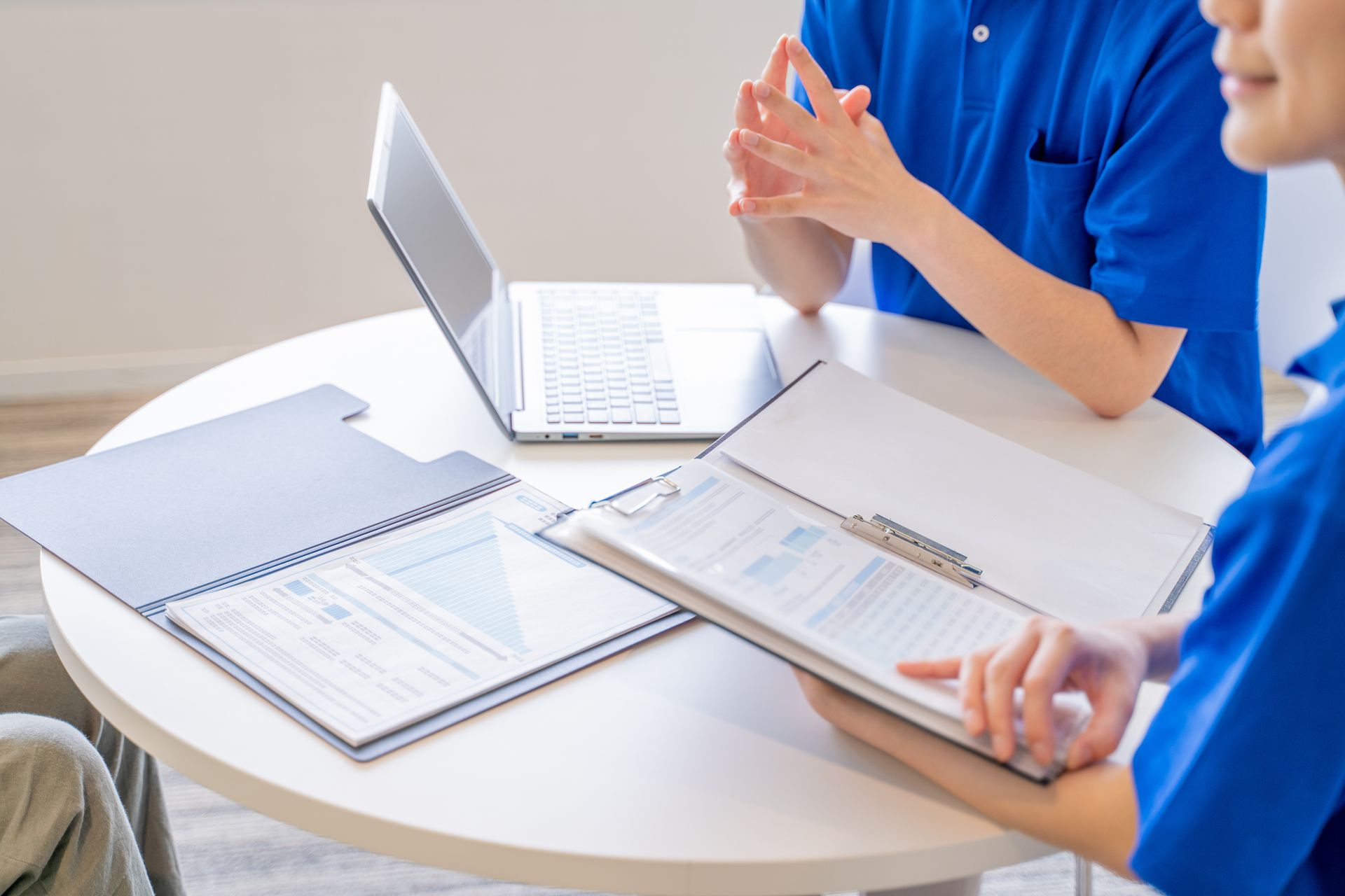 People in blue shirts review documents at a table with a laptop People in blue shirts review documents at a table with a laptop