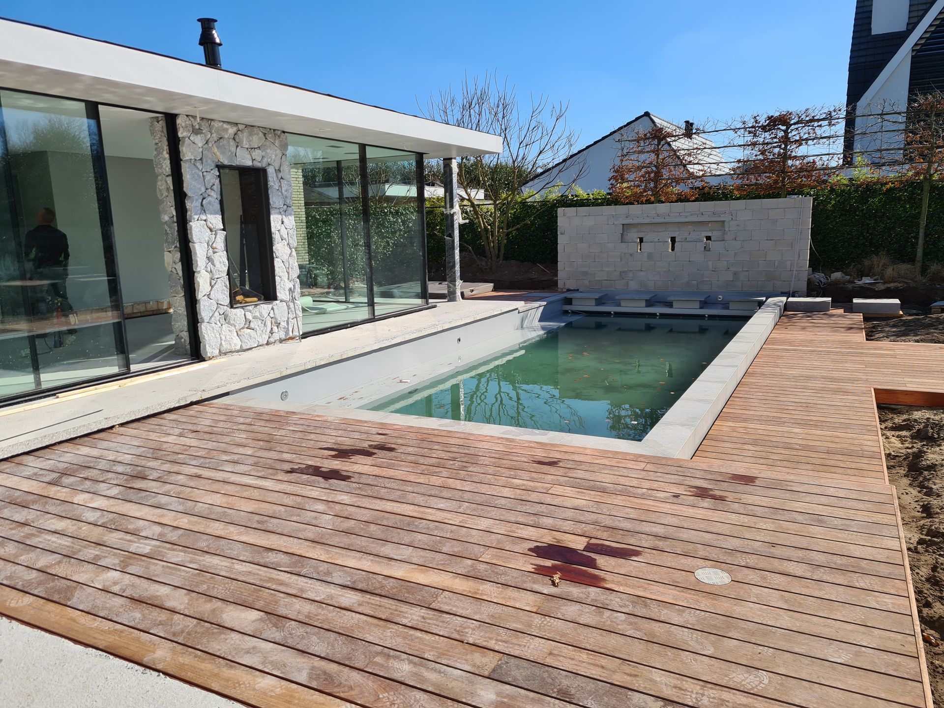 Een groot zwembad met een houten terras voor een huis.