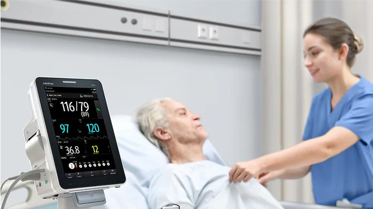 Nurse tending to a patient in a hospital room, monitoring vitals on a bedside device.