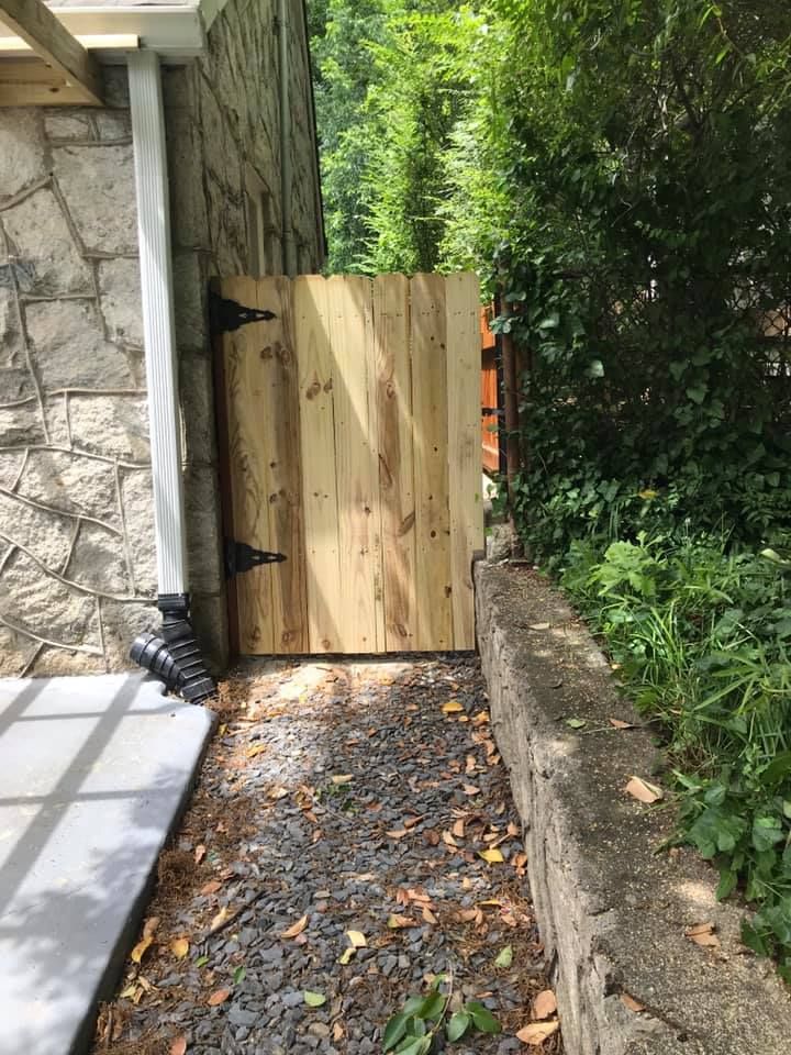 Wooden gate between stone wall and bushes, opening onto a gravel path.
