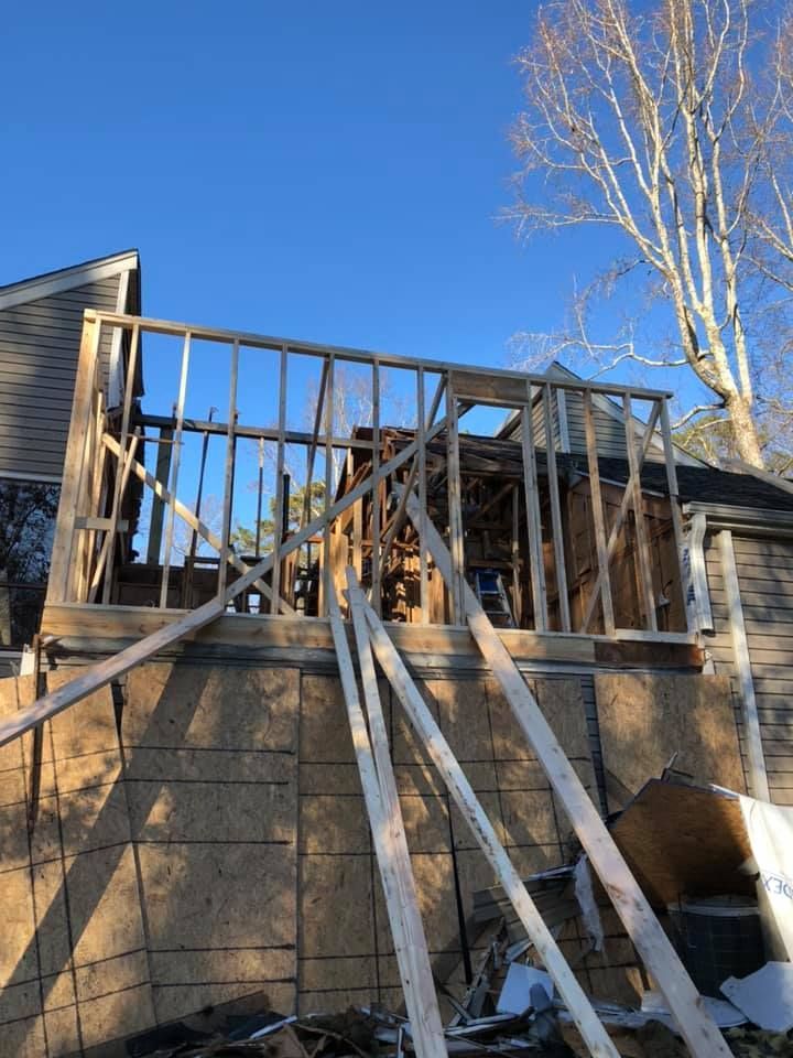 Framing for a wooden structure under construction against a backdrop of blue sky and a house.