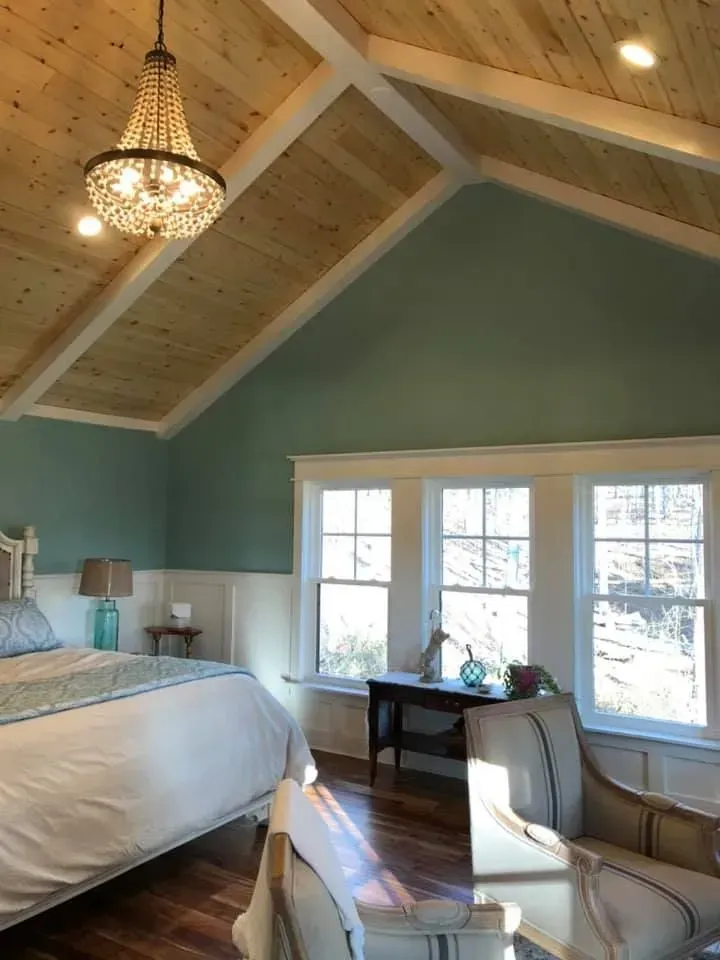 Bedroom with turquoise walls, wooden ceiling, crystal chandelier, bed, and windows.