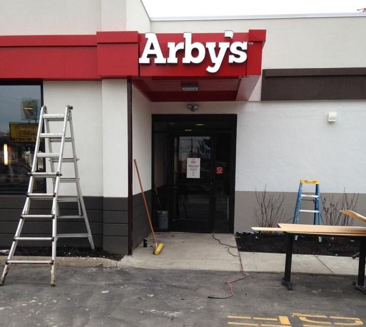 Arby's restaurant entrance under construction with a ladder, tools, and red awning.