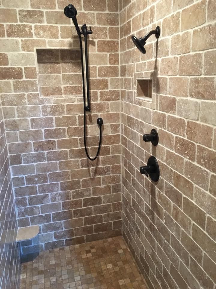 Brick-tiled shower with dark fixtures, including a handheld showerhead, and two recessed shelves.