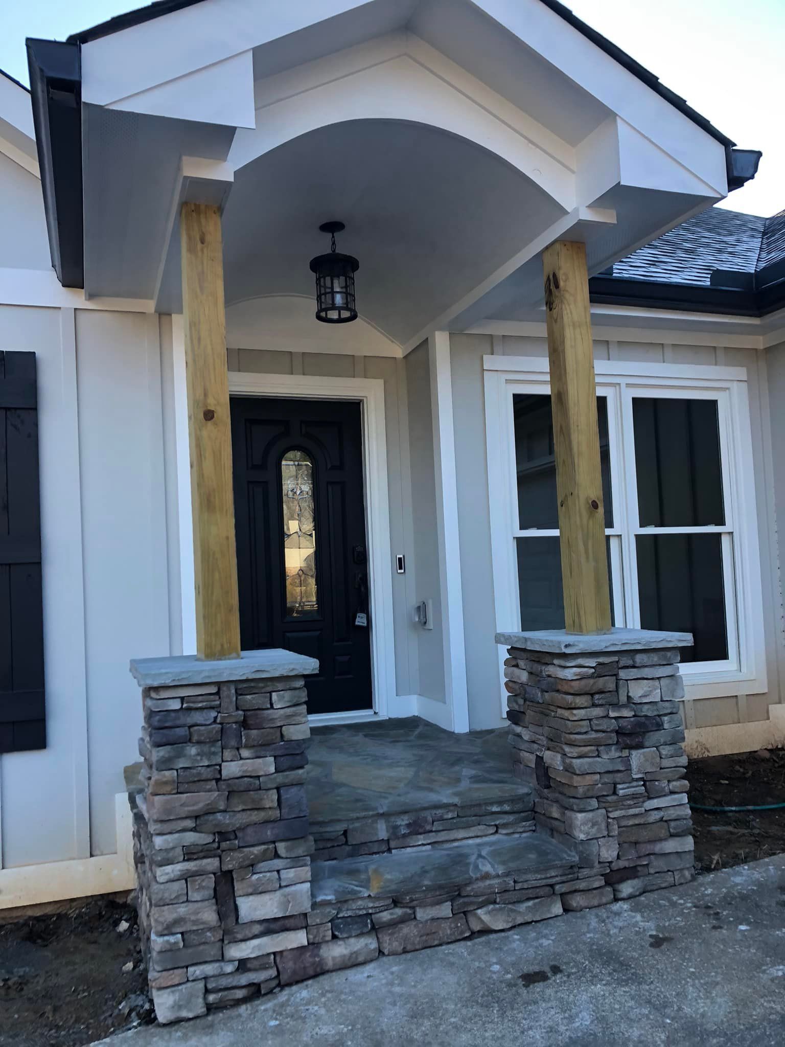 Front entrance of a house with stone columns, wood posts, black door, and a porch light.