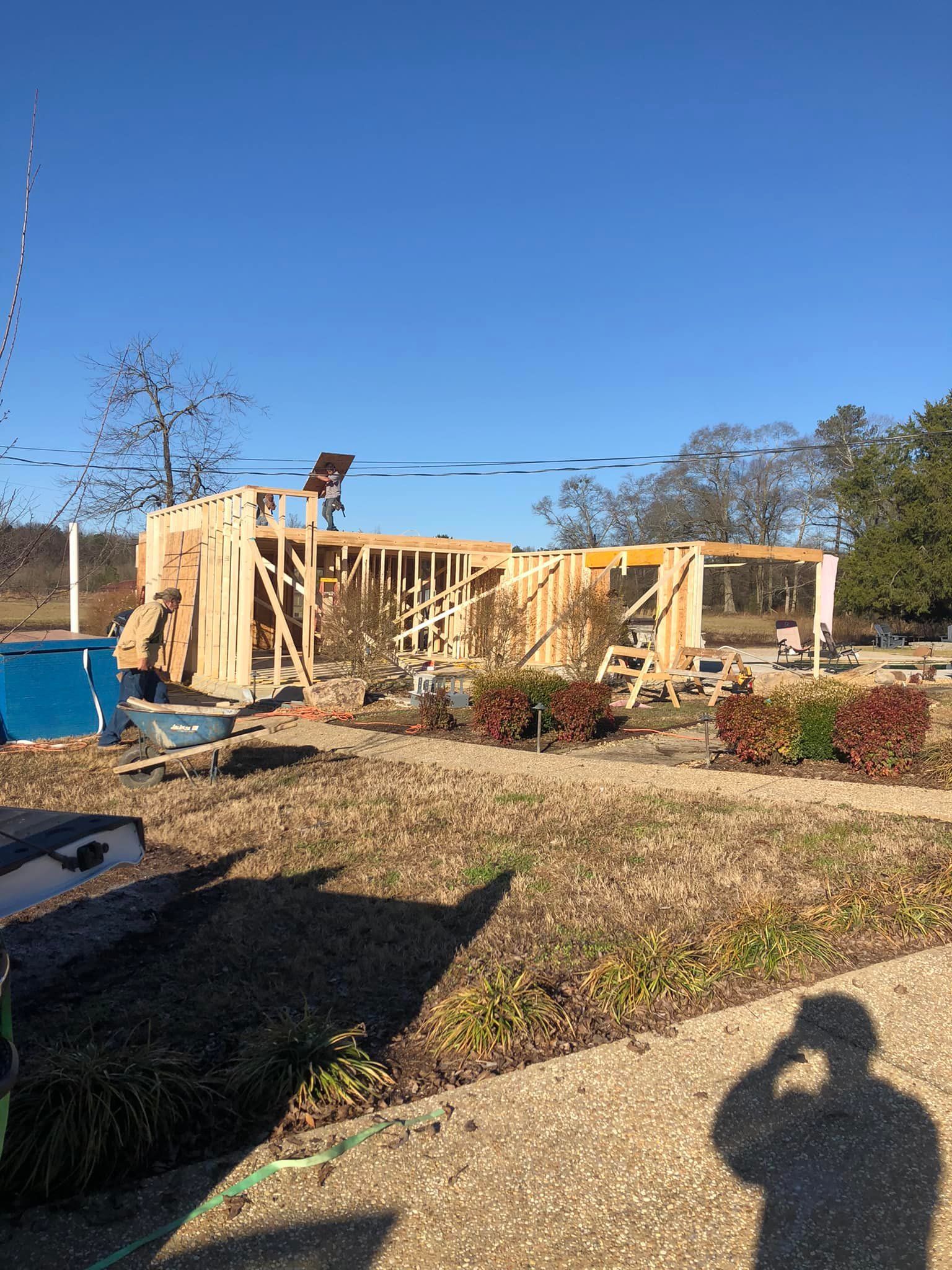 Framing of a building under construction on a sunny day. A worker is visible on the roof.