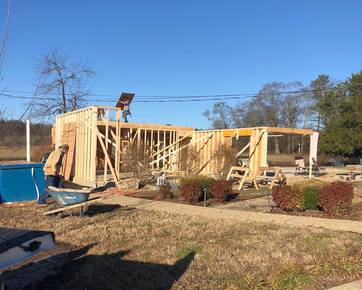 Framing of a new home under construction on a sunny day. A worker stands on the roof, surrounded by wood framing.