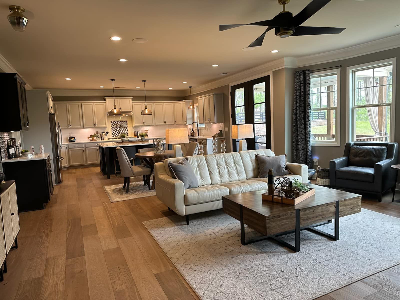 Open-concept living space with kitchen, dining area, and living room with neutral colors, wood floors, and dark accents.