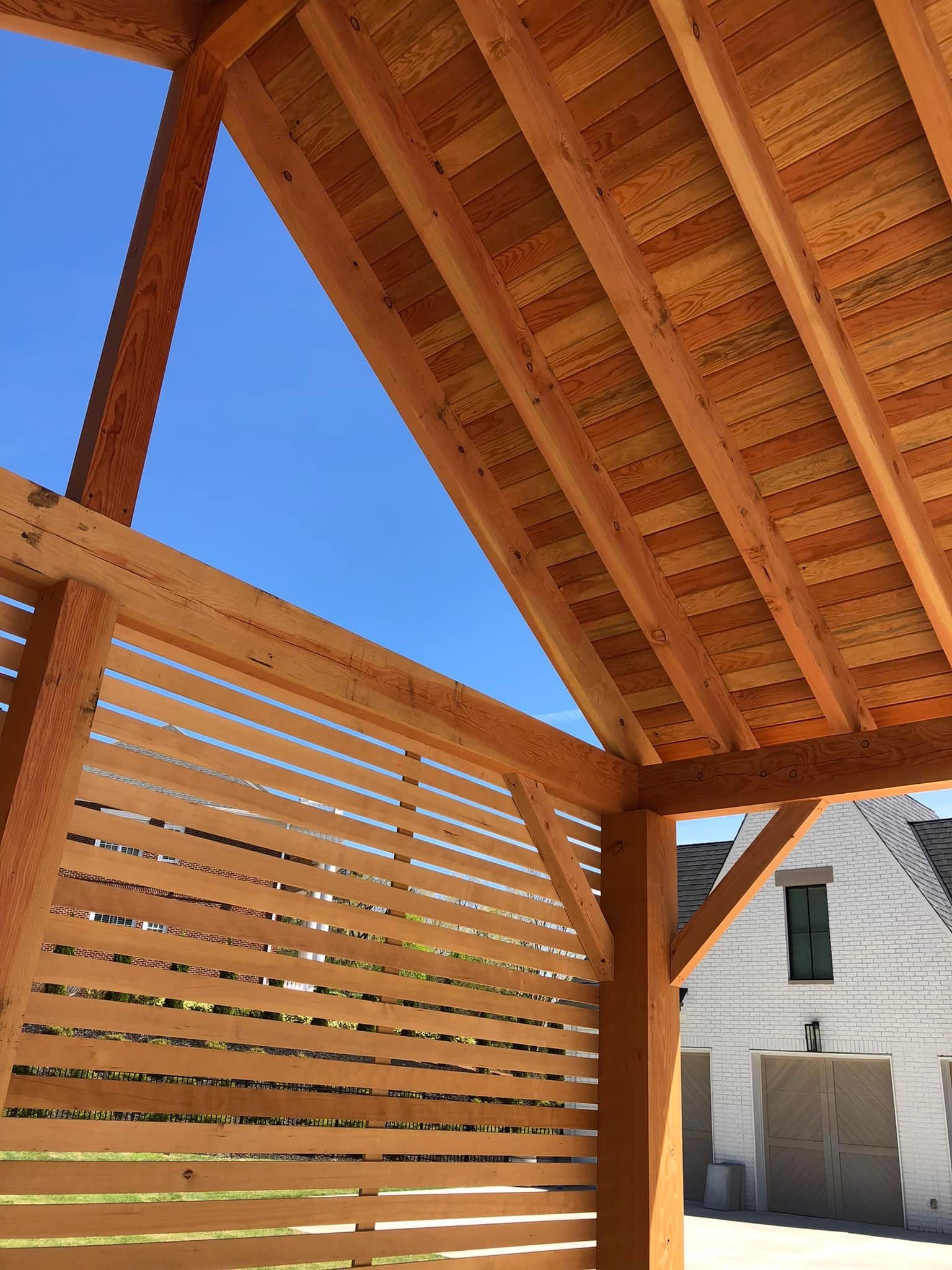 Wooden structure with a slatted wall, beams, and ceiling slats, against a bright blue sky.