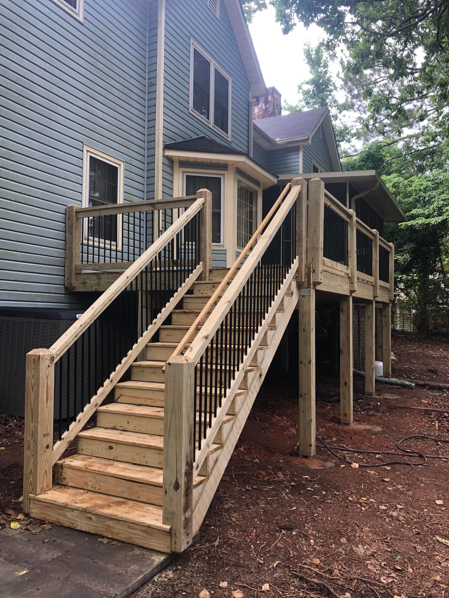 Wooden deck with stairs leading to a house with blue siding. Black iron railings.