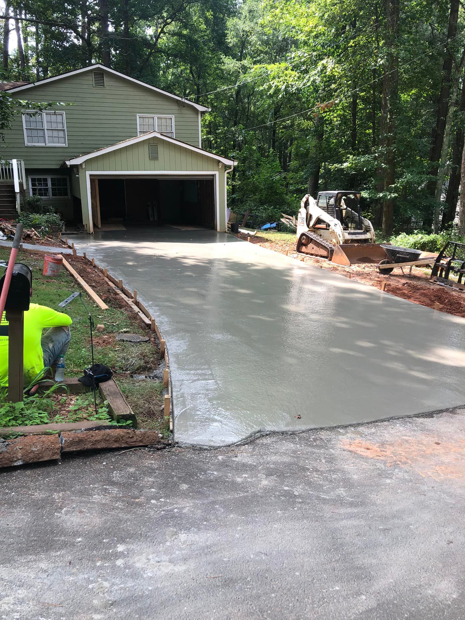 New concrete driveway being poured; house in background; construction worker.