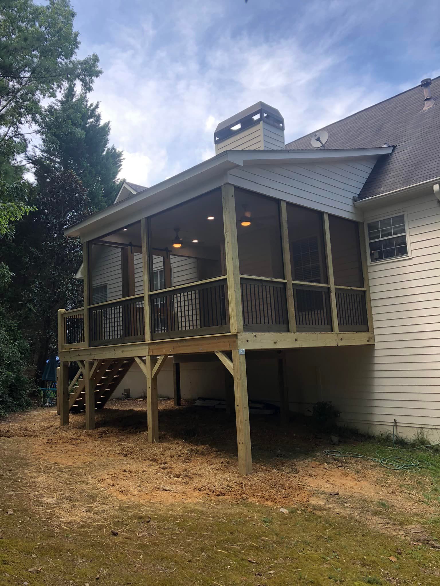 Screened porch with wooden deck, attached to a house, with a stairway and a gravel ground.
