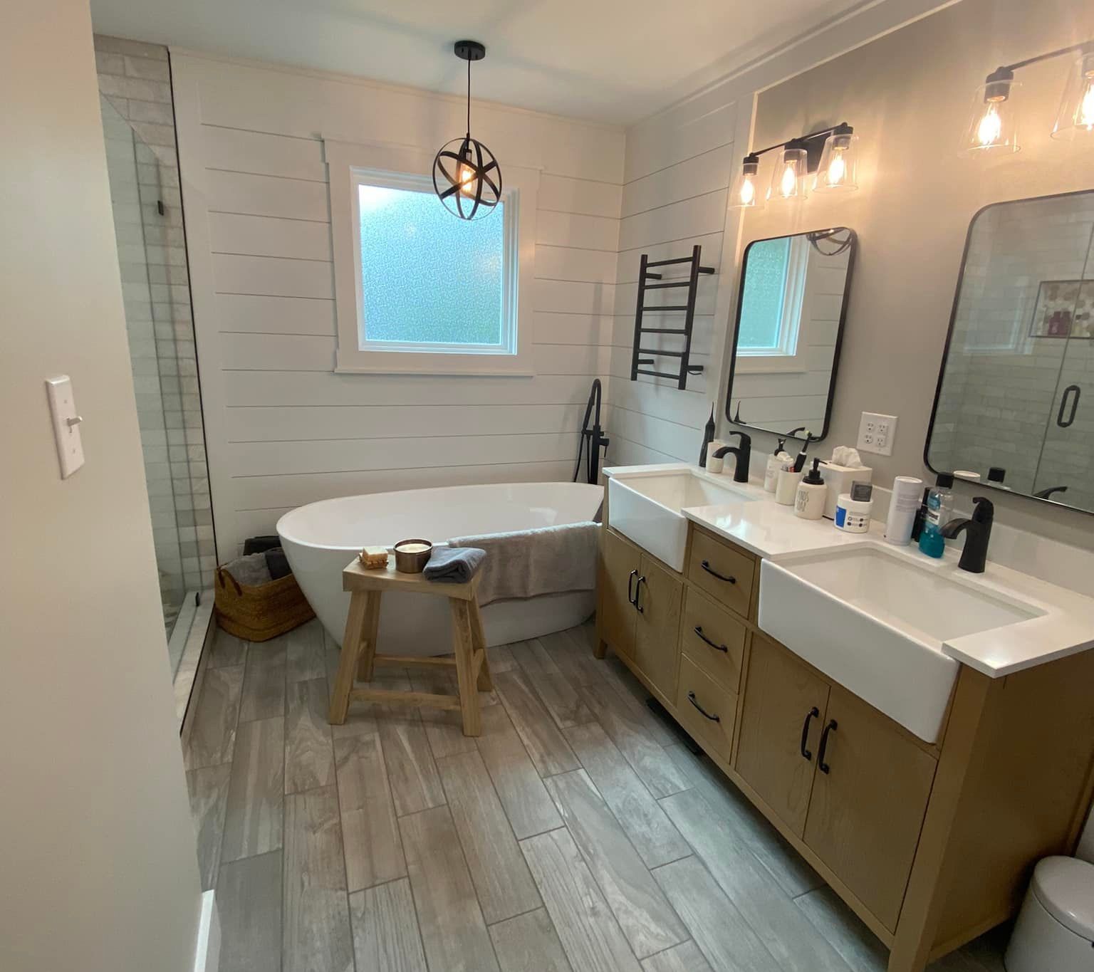 A modern bathroom with a freestanding tub, wooden vanity with double sinks, and a light-colored wood-look floor.