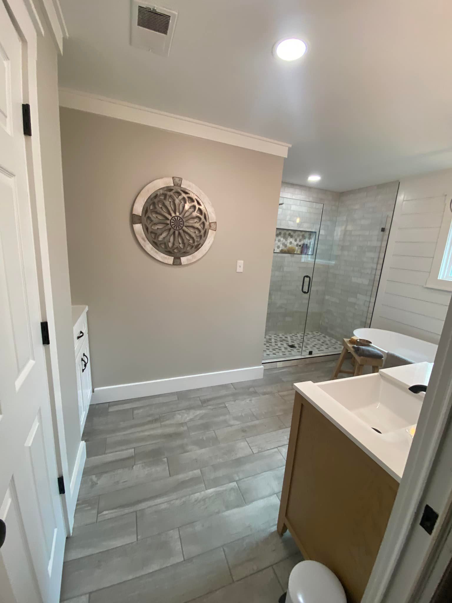 Bathroom with a wooden floor, tan walls, a glass shower, and a decorative wall piece.