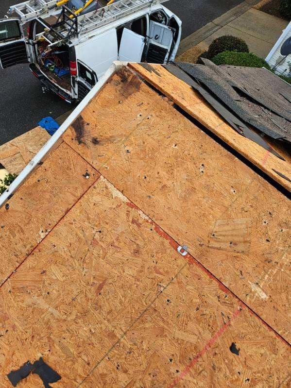 A partially shingled roof with exposed plywood and a work van in the background.