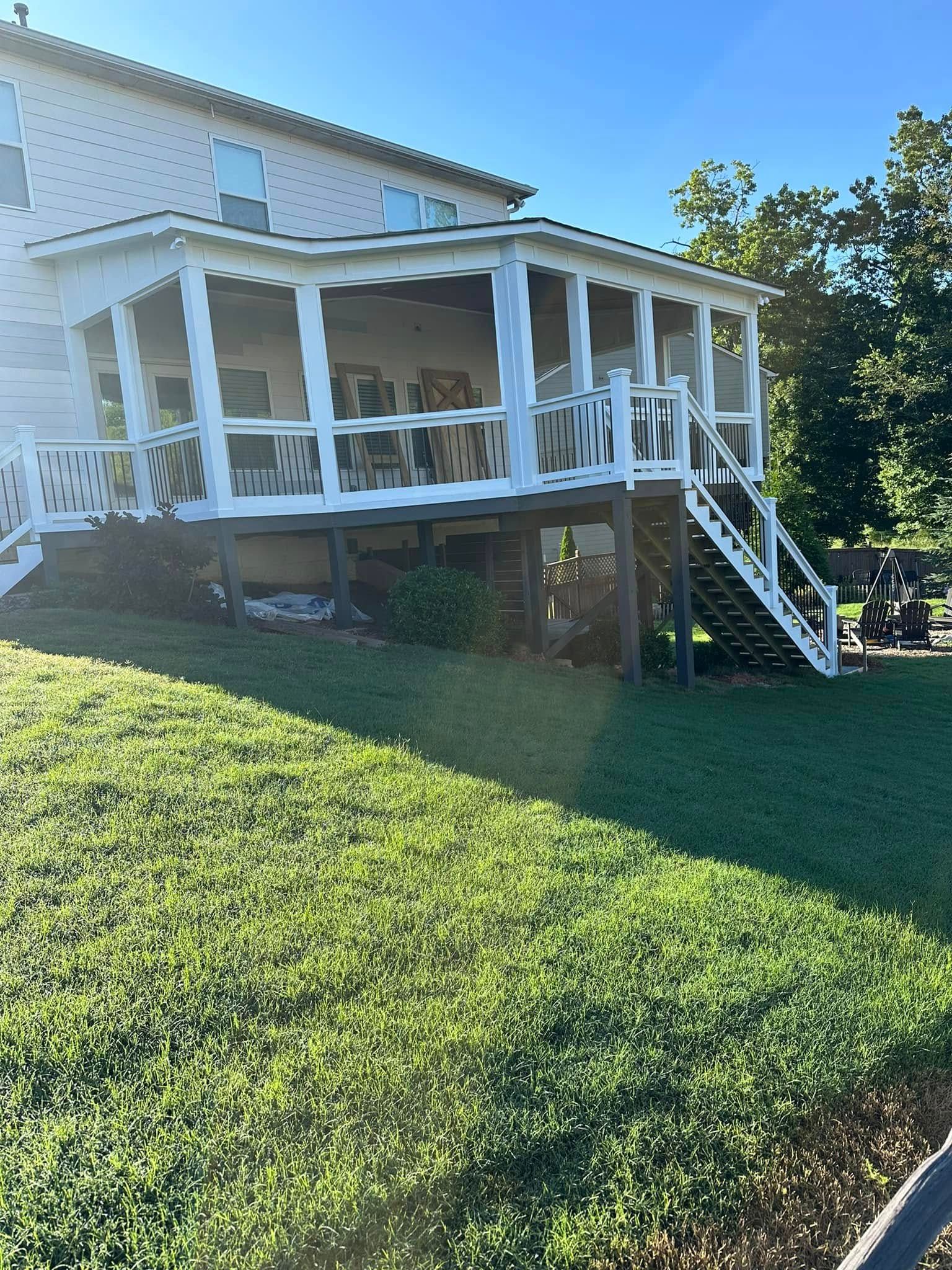 A white porch on a two-story house with stairs on a grassy hill under a blue sky.