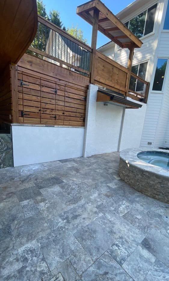 Patio with a hot tub, wooden deck, and white stucco wall in a residential setting.