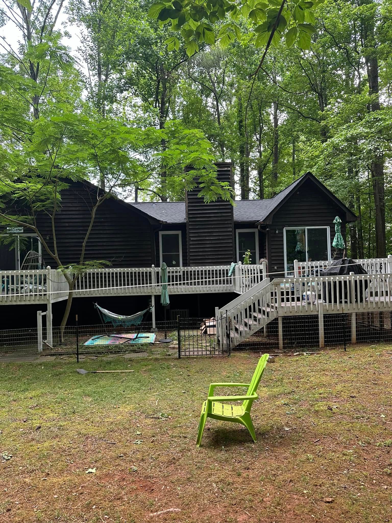 A dark brown cabin with a white deck, set in a wooded area with a green chair in the foreground.