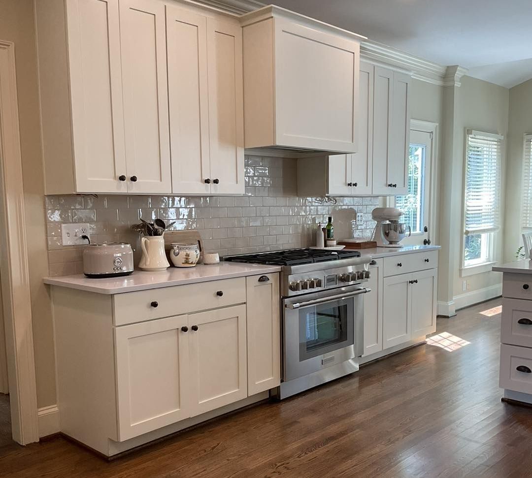 Creamy white kitchen with wooden floors, stainless steel appliances, and white cabinets.