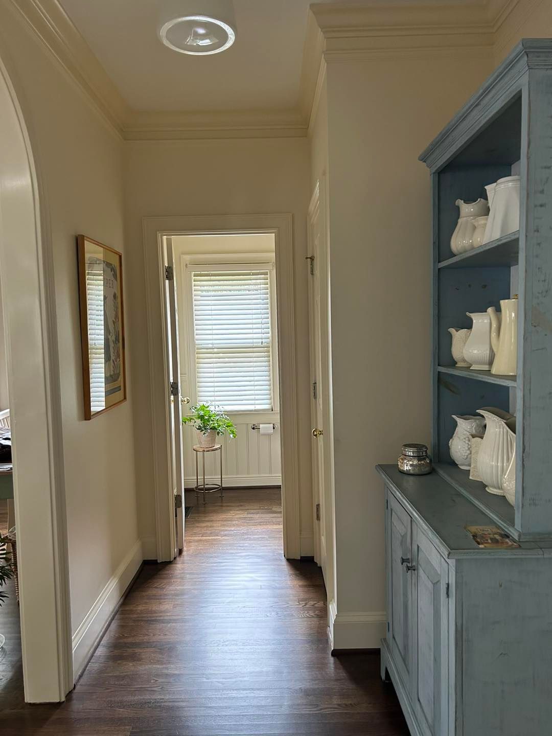 Hallway with dark wood floor, cream walls, blue cabinet with white dishware.