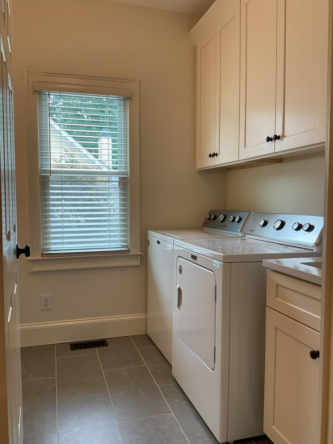 Laundry room with a washer and dryer, white cabinets, a window with blinds, and gray tile floor.