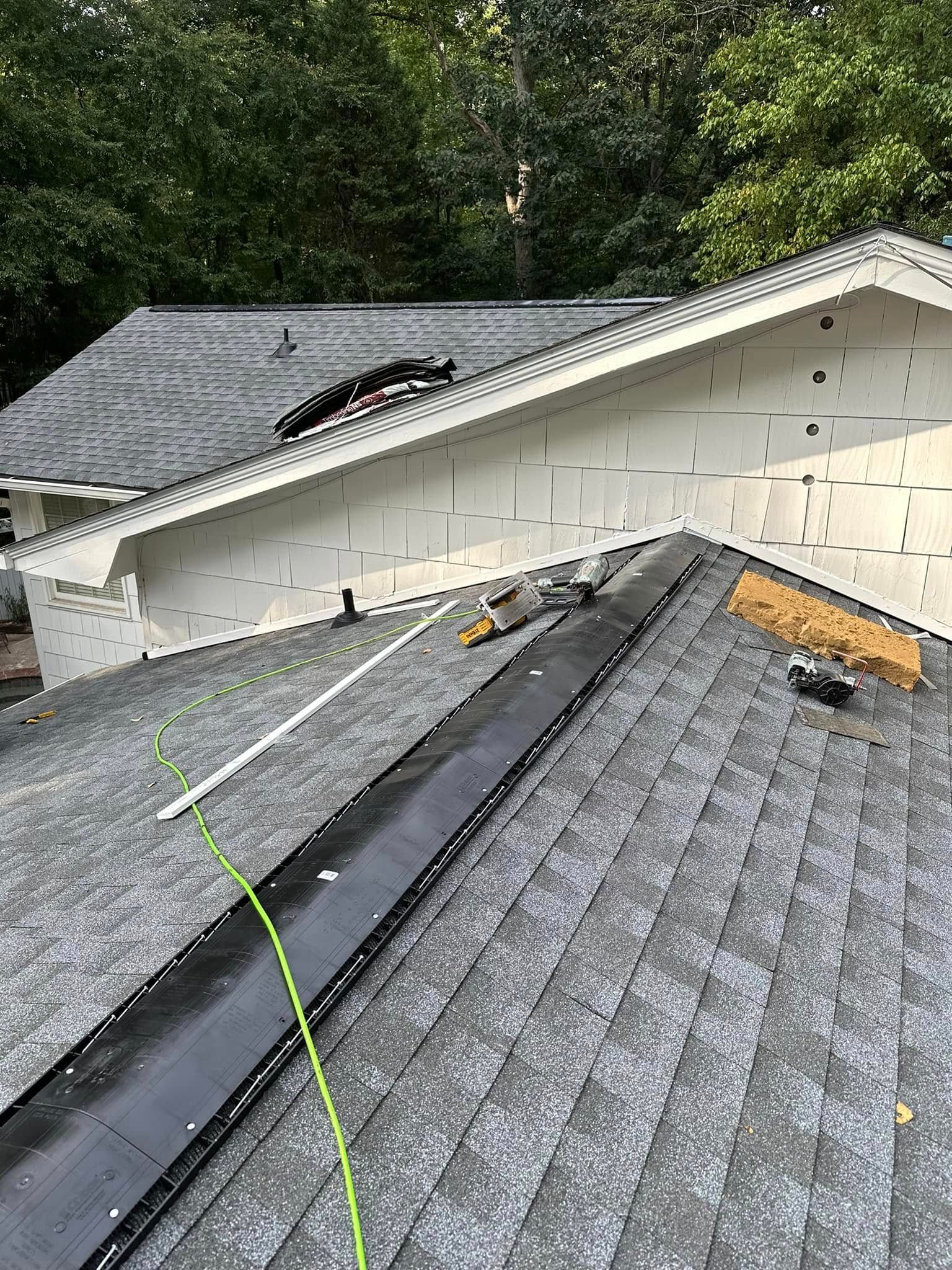 Rooftop with new black sealant installed around a roof valley and tools, and the gable end of the house is being worked on.