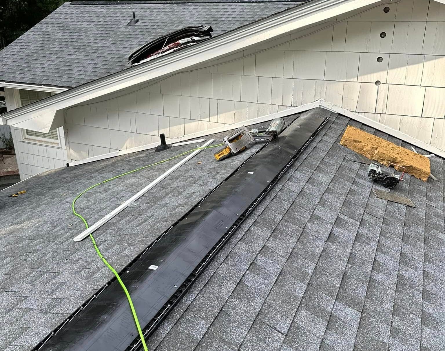 Rooftop view of a house under construction; black roofing shingles and a long trough with tools; white siding.