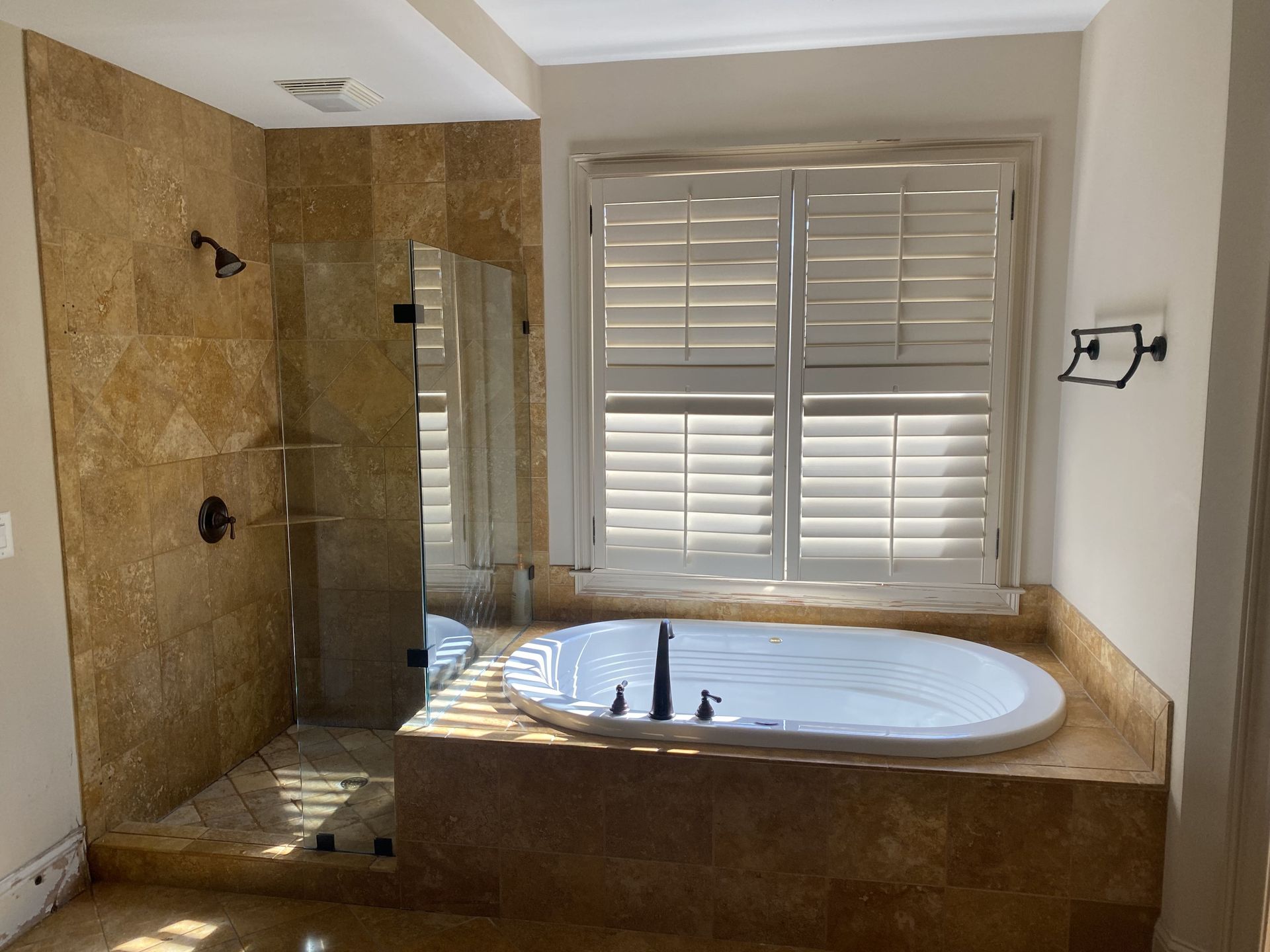 Bathroom with a bathtub, shower, marble walls, and window with shutters.