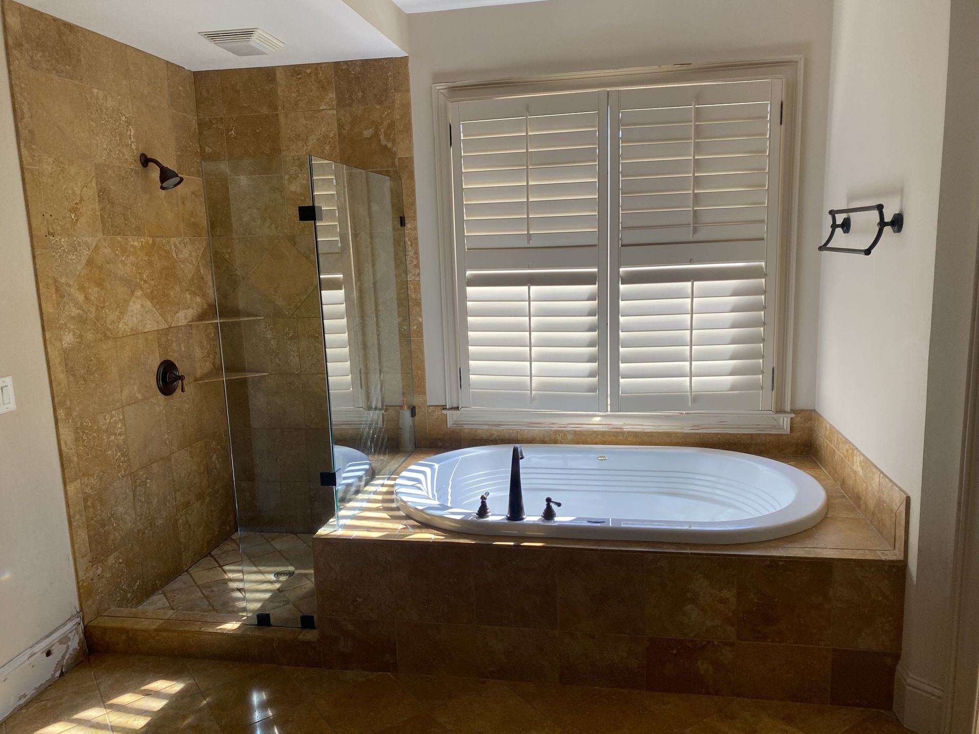 Bathroom with tiled shower, tub, and window with shutters.