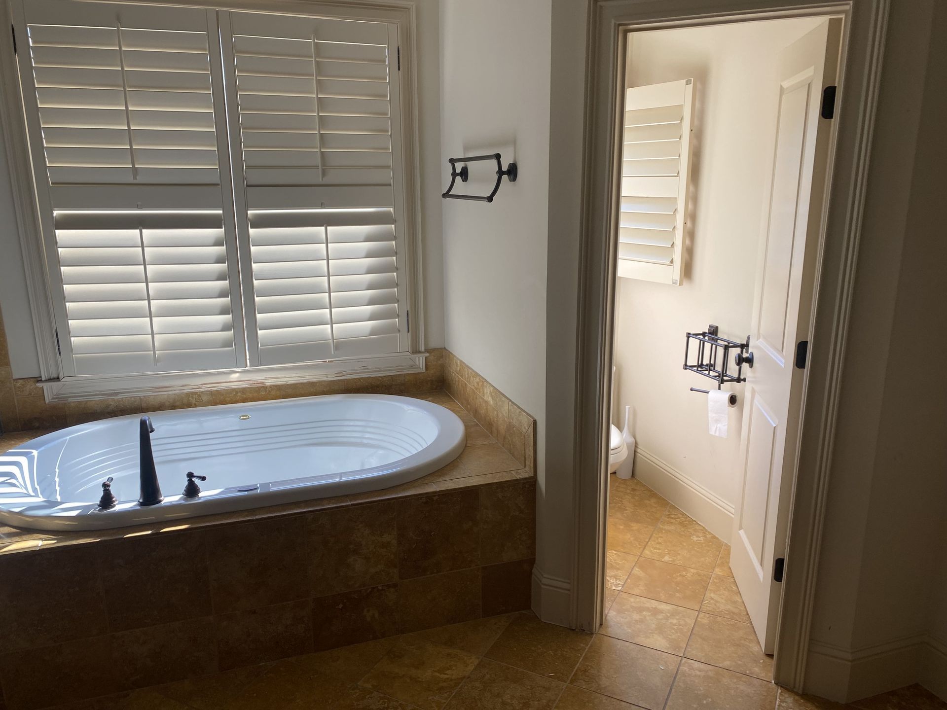 Bathroom with a white bathtub, shuttered window, and a door leading to a toilet room.
