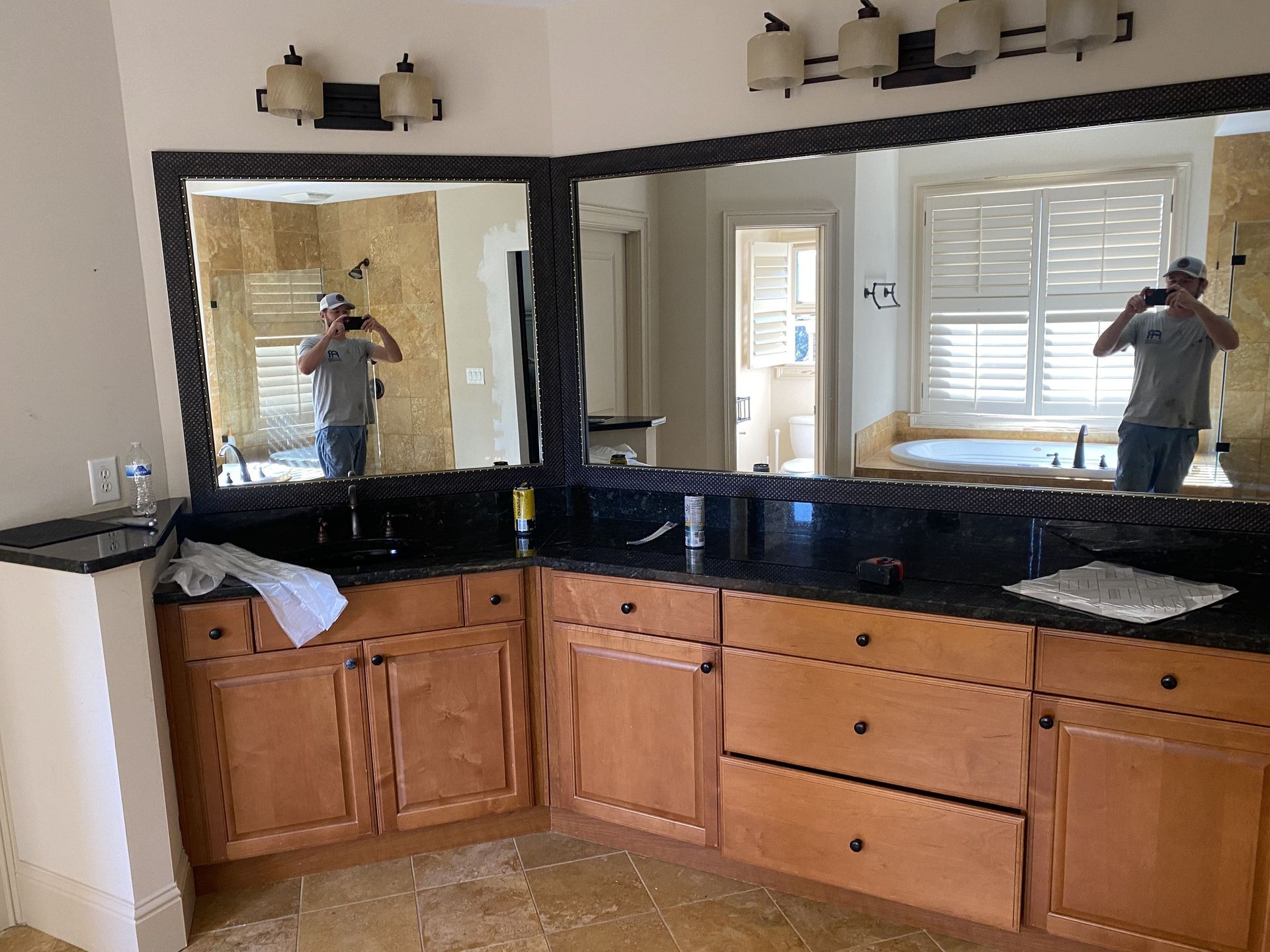 Bathroom with wood cabinets, black countertops, and large mirrors reflecting the interior.