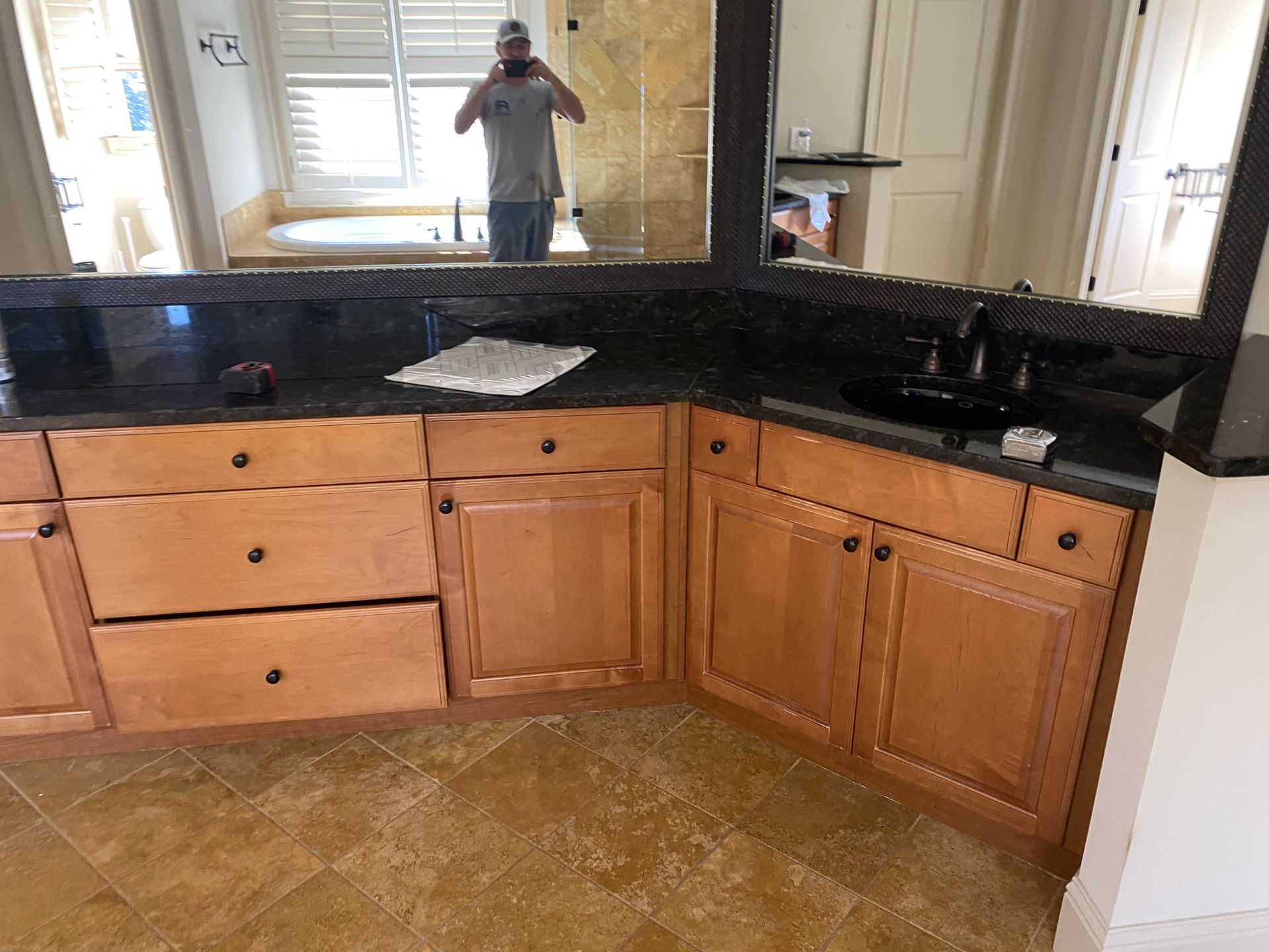 Bathroom vanity with black countertop and light wood cabinets. A person is reflected in the mirror.