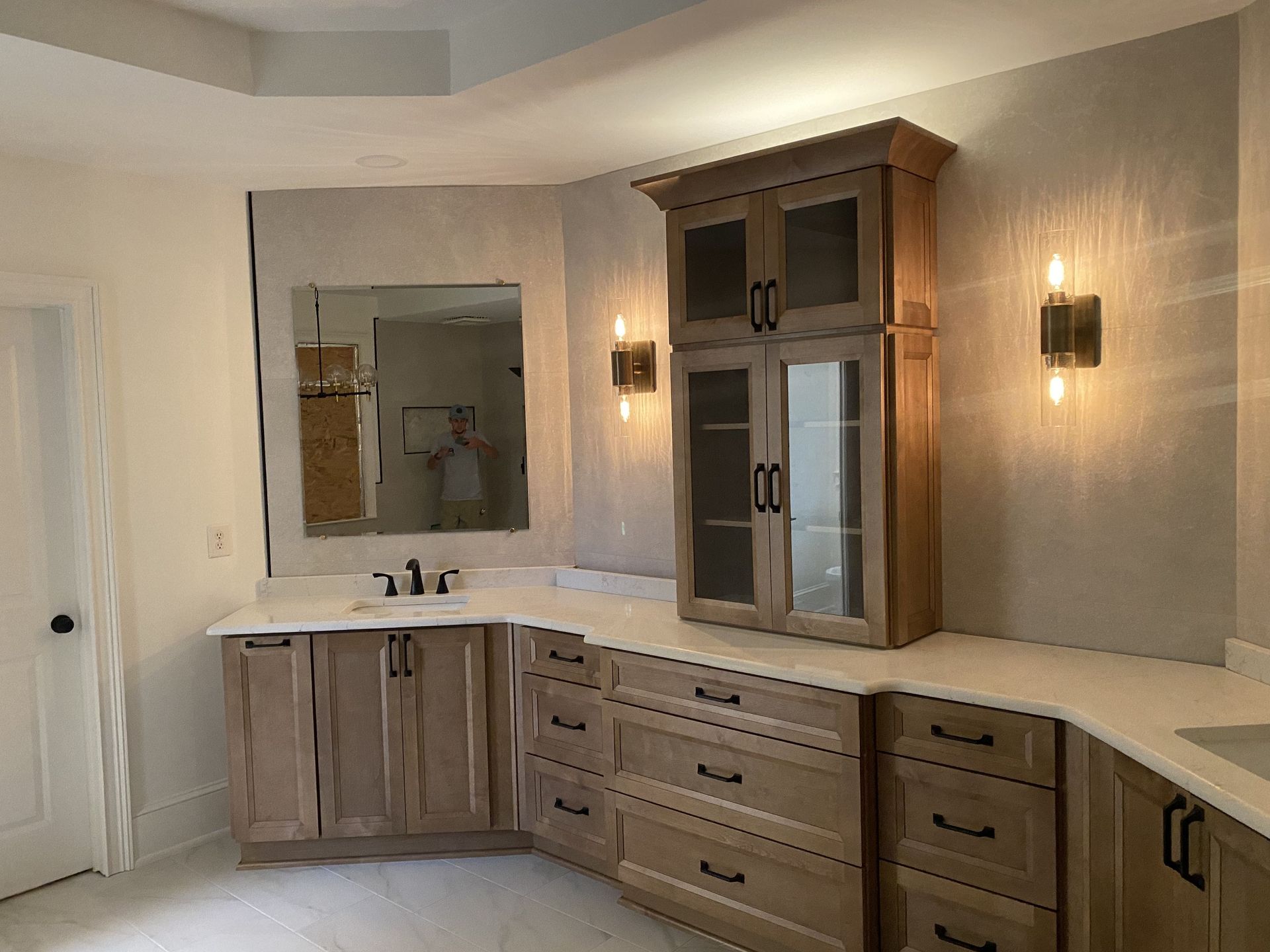 Bathroom with light wood cabinets, countertop, mirror, and sconces.