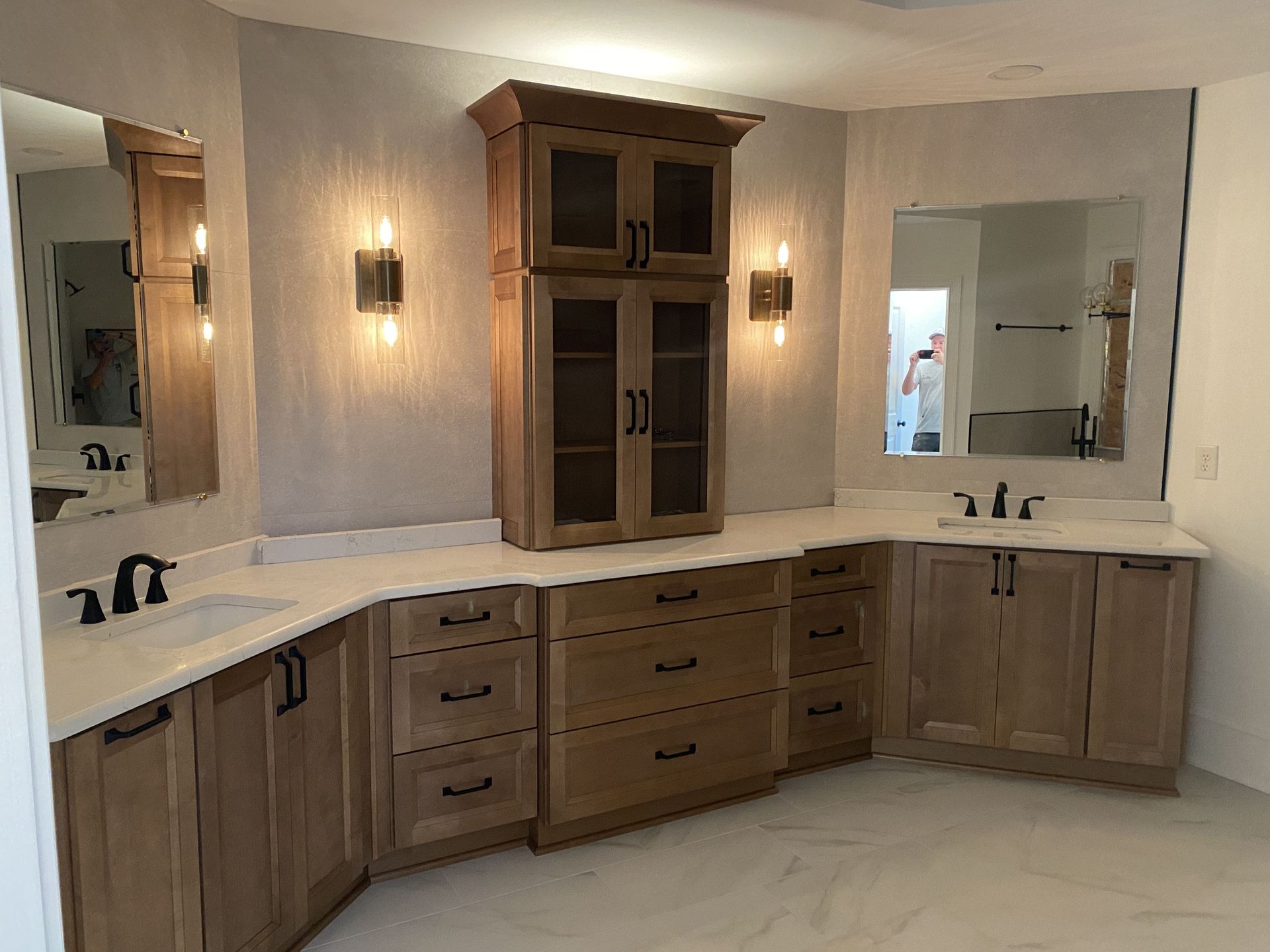 Bathroom with wooden cabinets, sinks, mirrors, and a central cabinet with glass doors.