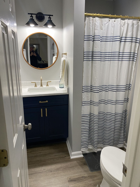 Small navy bathroom with a sink, mirror, shower, and toilet.