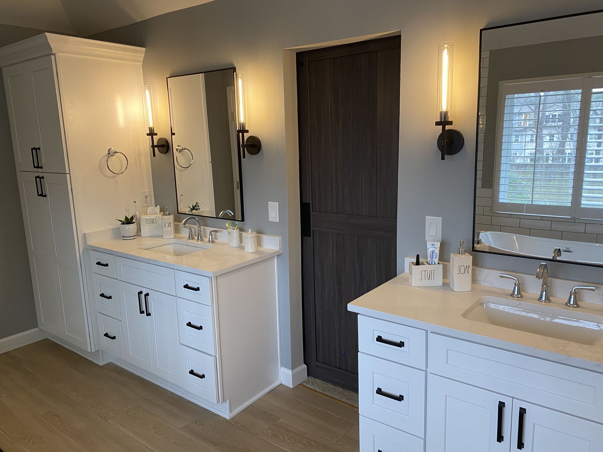 Bathroom with white cabinets, marble countertops, mirrors, and sconces. Doorway on the right.